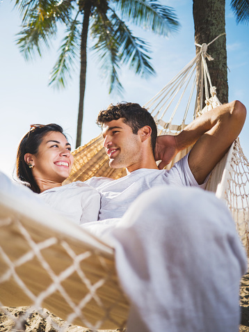 Happy Hispanic couple relaxing in hammock and communicating.