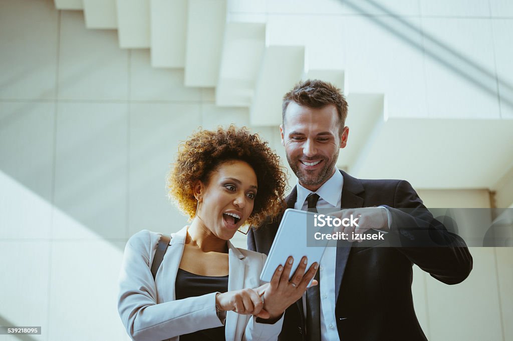 Businesswoman and businessman using a digital tablet Afro american businesswoman standing against white wall and using a digital tablet with her business colleague. Surprise Stock Photo