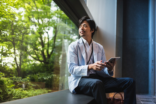 A Japanese businessman working on a project using digital tablet and looking outside the window