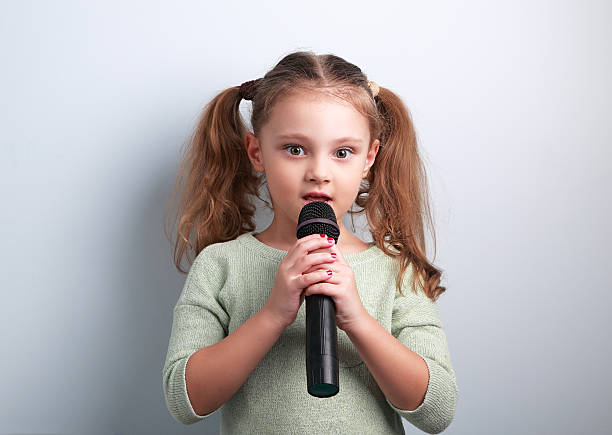 istock Cute fun kid girl singing in microphone on blue background 539224918