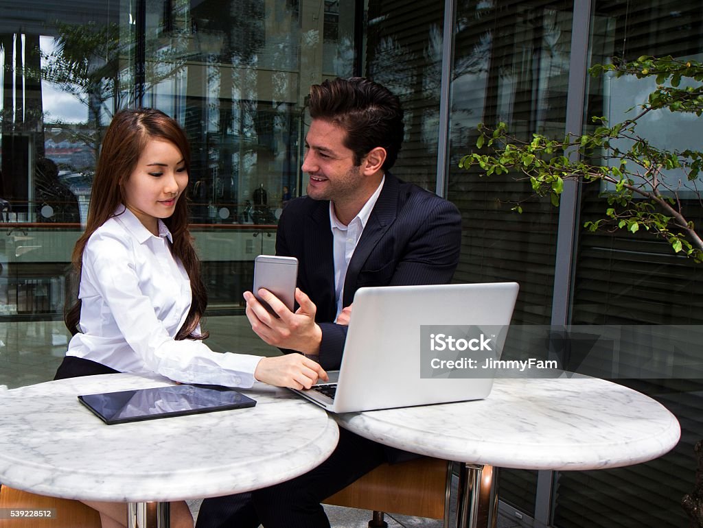 Multiracial Business Team working outdoors Multiracial Business Team working outdoors. Chinese Business woman discussing business deal with Caucasian Business man on a laptop computer Adult Stock Photo