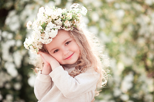 Smiling kid girl posing with flower wreath outdoors. Looking at camera. Childhood.