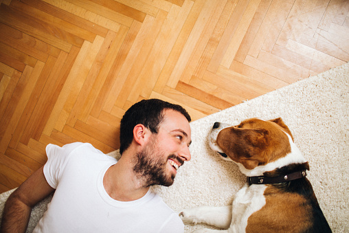 Smiling men and his dog lying on the floor in their living room