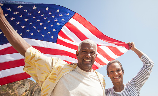 African American Senior couple carrying American flag on beach