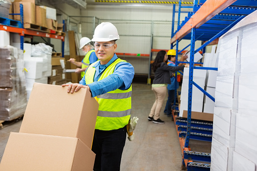 Blue collar worker moving boxes in busy distribution warehouse