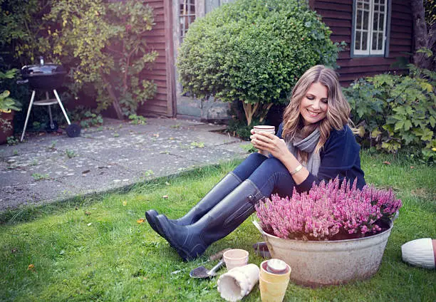 Attractive woman wearing autumn clothes and gum boots planting flowers in garden.