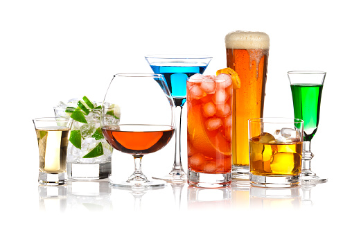 Colorful lineup of popular bar drinks, including caipirinha, brandy, beer, scotch, martini and various liqueurs. The drinks are arranged in a row and backlit. Visible reflection of the glasses in the foreground.