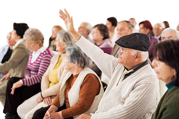 Large group of seniors at training. Focus is on senior man raising his hand ready to answer the question. Isolated on white.