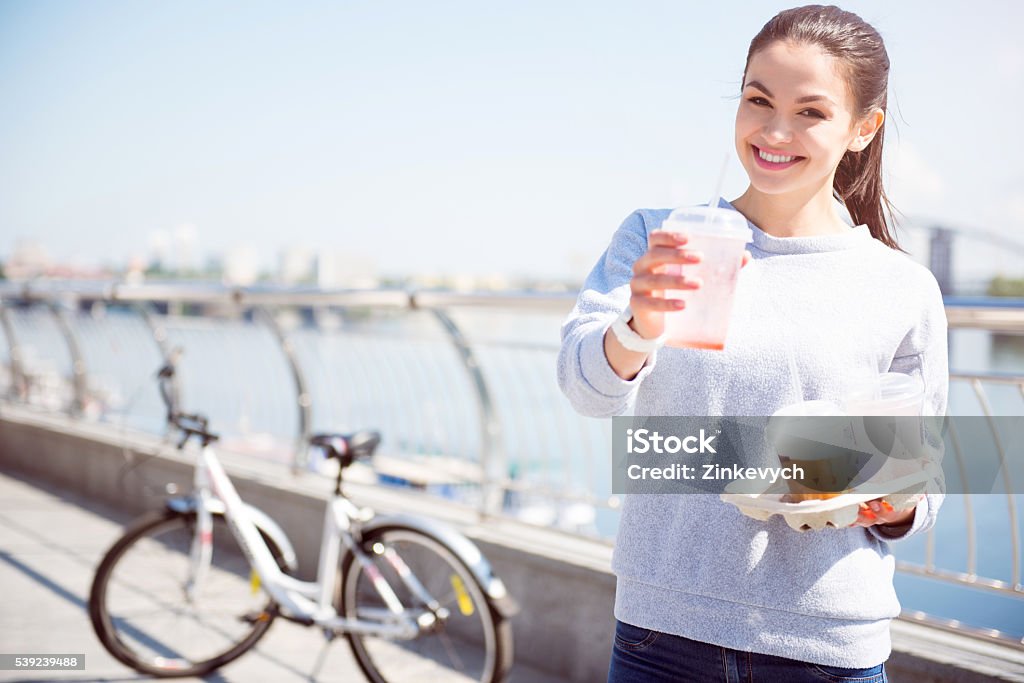 Smiling woman giving a beverage Take it. Smiling charming young woman giving a beverage while looking at the camera and standing in front of the bicycle Adult Stock Photo