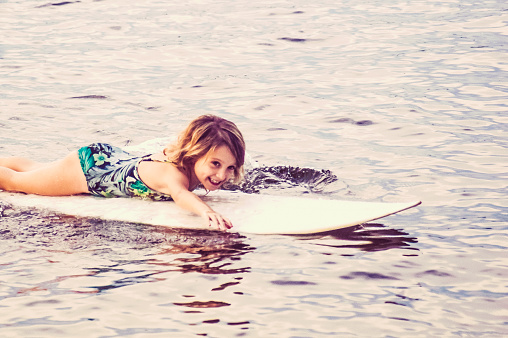 LIttle girl paddles out on a surfboard and smiles
