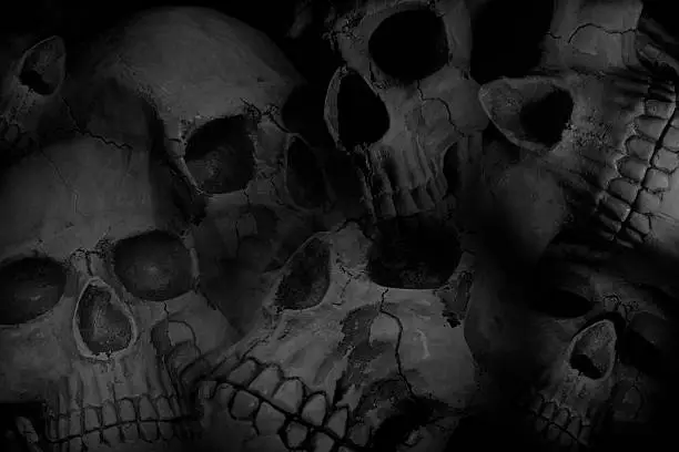 Pile of human skulls put together composite style with blurred edges and slight transparency on black.