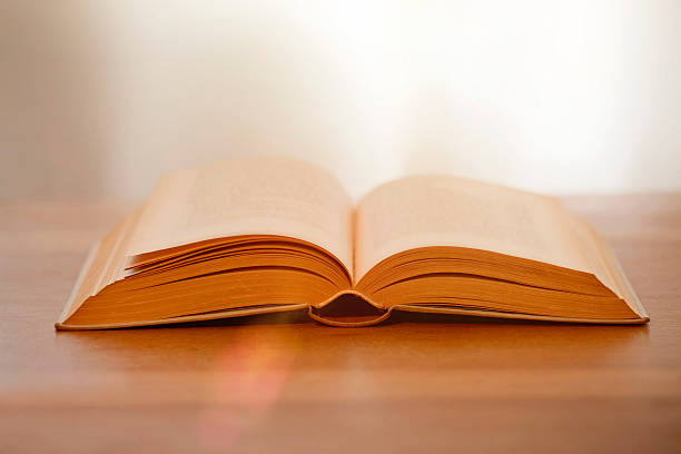 istock Old book opened on wooden table with light 539244493