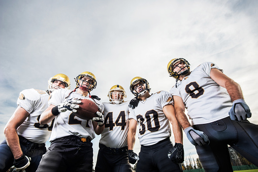 Low angle view of five American football players standing on the playing field and looking away.   