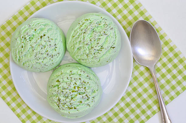 three  scoops of green ice cream, pistachio, woodruff, peppermint or kiwi flavor,  on white plate with white and green checkered napkin, on white backgroung,  close up, vertical, horizontal, full frame, flat lay