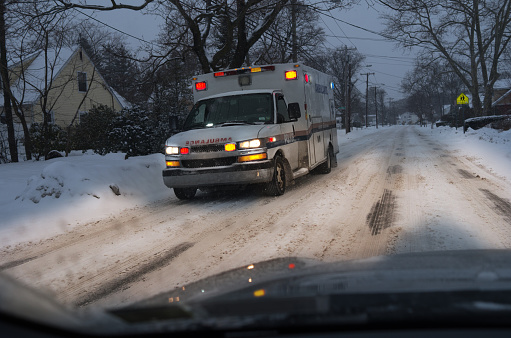 Ambulance driving on suburban snow covered road at night.