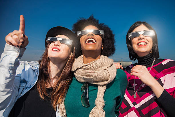 Group of friends looking to a solar eclipse Group of female friends have fun together during a solar eclipse event. Their looking and pointing to the sun wearing the typical glasses normally used to watch a solar eclipse. eclipse stock pictures, royalty-free photos & images