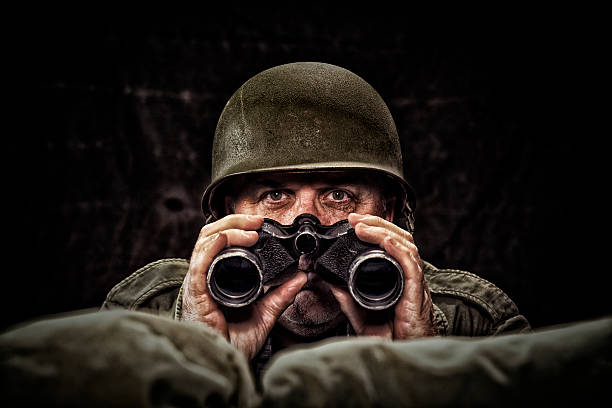Vintage Army Soldier with binoculars in a fox hole Vintage Army Soldier holding binoculars looking over the sand bags of his fox hole, with low key lighting binoculars photos stock pictures, royalty-free photos & images