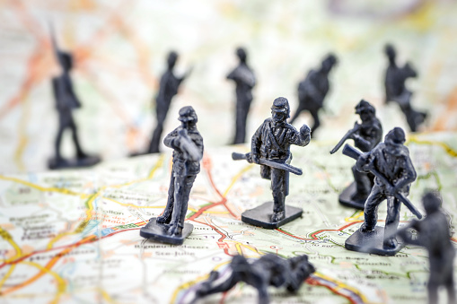 Concept of war, with little soldier toy running on battlefield of conflict with weapon in hands in selective focus with blurred soldier in background, placed on a military map. Macro shot.
