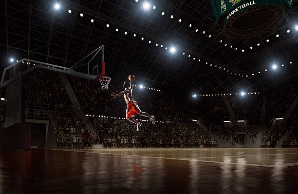 Basketball player makes slam dunk Close up image of professional basketball player about to do slam dunk during basketball game in floodlight basketball court slam dunk stock pictures, royalty-free photos & images