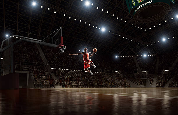Basketball player makes slam dunk Close up image of professional basketball player about to do slam dunk during basketball game in floodlight basketball court slam dunk stock pictures, royalty-free photos & images