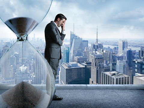 A businessman, standing on a observation deck high above the city of New York, holds his head in his hands 