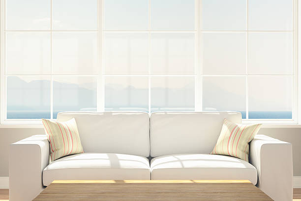 A living room interior with white modern linen sofa and light green pillows, wooden rustic coffee table towards beautiful sea and mountain view.