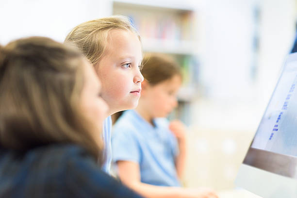 UK Junior school girl working on computer Teacher working with children using computers teacher classroom child education stock pictures, royalty-free photos & images