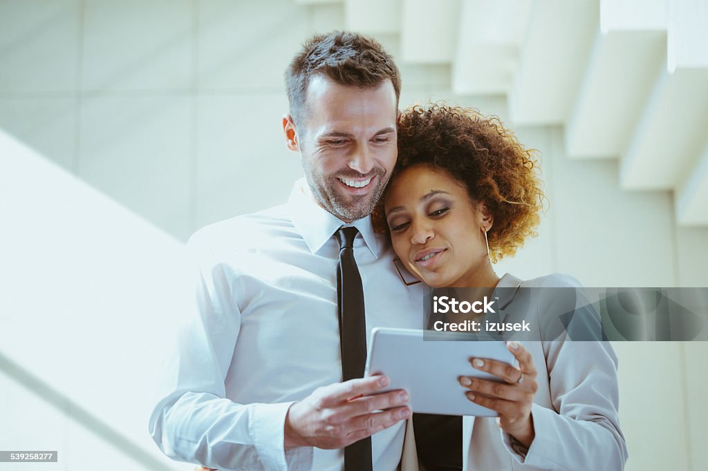 Elegance couple using a digital tablet Afro american woman embracing with attractive man, using a digital tablet together against white staircase. Couple - Relationship Stock Photo
