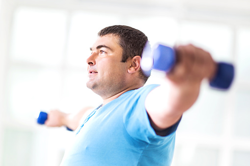 Side view of young overweight man exercising with dumbbells.  