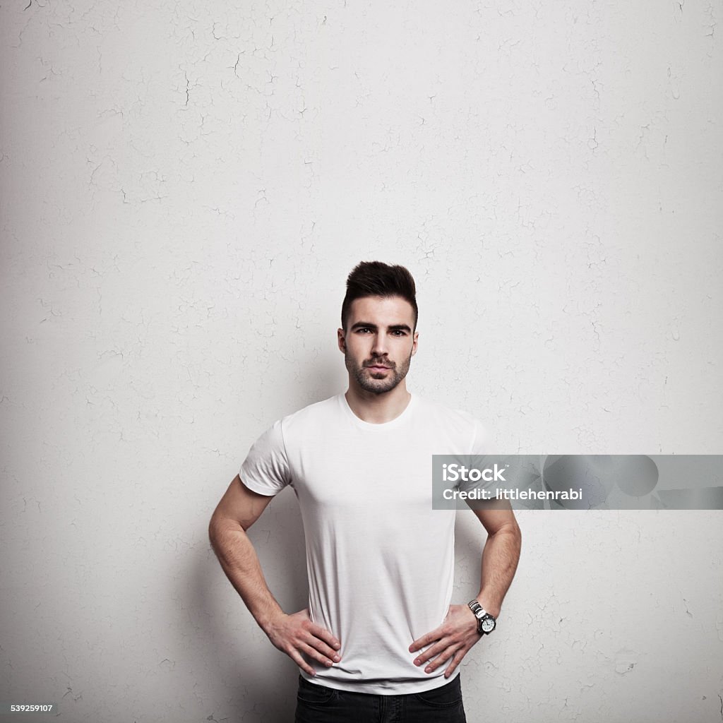 Man in blank t-shirt and wall background Serious man standing near grunge wall in blank t-shirt, front, studio Activity Stock Photo