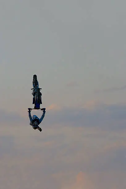 A male freestyle FMX motocross rider does a Tsunami Backflip trick off a big jump at night. 
