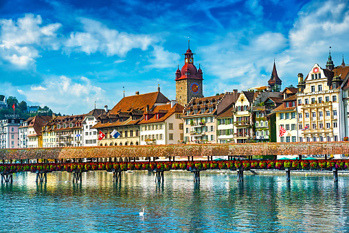 Beautiful Cityscape of old town Lucerne, visible are the river Reuss waterfront of Lucerne with the famous Kapellbrucke bridge originally built in 1333, traditional swiss buildings, churches, restaurants, coffee bars, hotels, beautiful cloudscape and reflection in the water.  