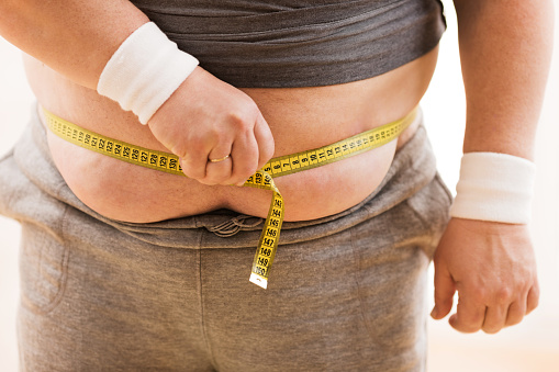 Unrecognizable fat person measuring waist.