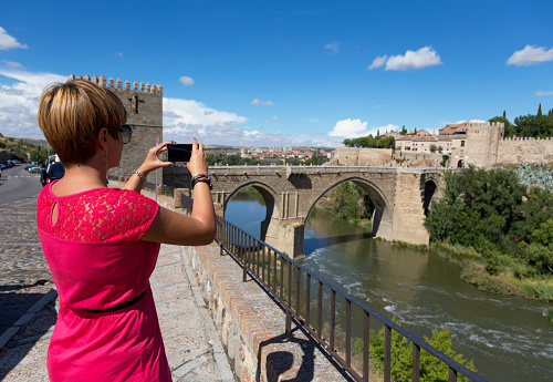 Female tourist photographing Puente de San Martini, Toledo, Spain using smart phone, copy space