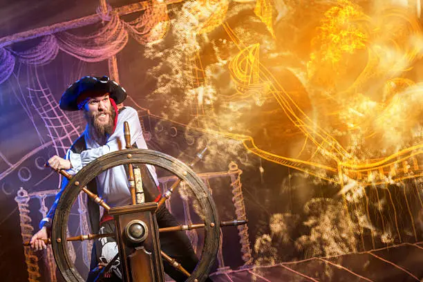 Brave buccaneer standing at the helm of a pirate ship. Chalk drawing of a pirate ship floating in the sea on the background