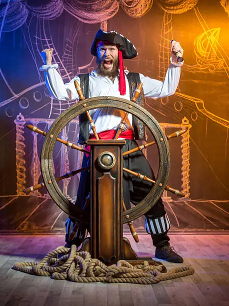 Comical pirate standing at the helm of a pirate ship. Chalk drawing of a pirate ship floating in the sea on the background
