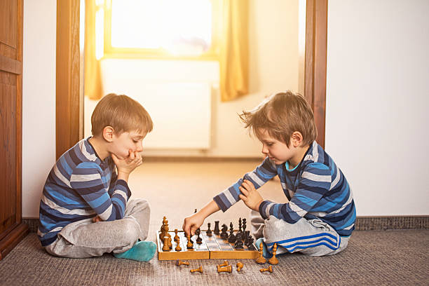 Little brothers playing chess on the floor.