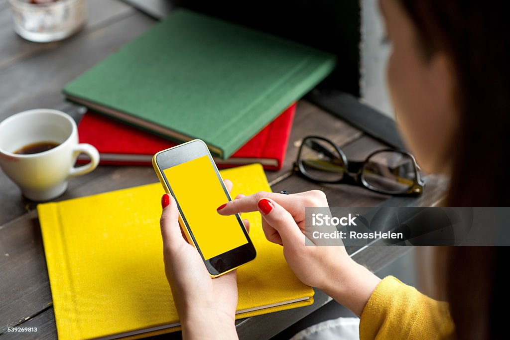 Using smart phone Woman using smart phone on the table with colorful books. Phone with empty screen for your application Adult Stock Photo