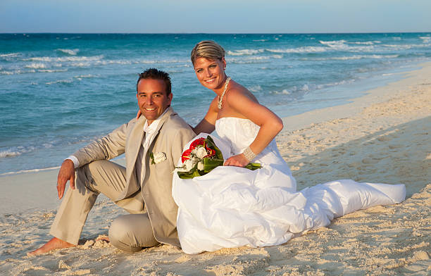 Couple Just Married Sitting On The Beach At Sunset stock photo