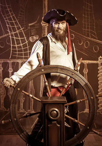 Brave pirate standing at the helm of a pirate ship. Chalk drawing of a pirate ship floating in the sea on the background
