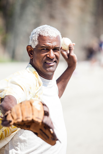 African American Senior Man Playing Catch on beach with baseball glove and baseball, throwing the ball to somebody who is off-camera.