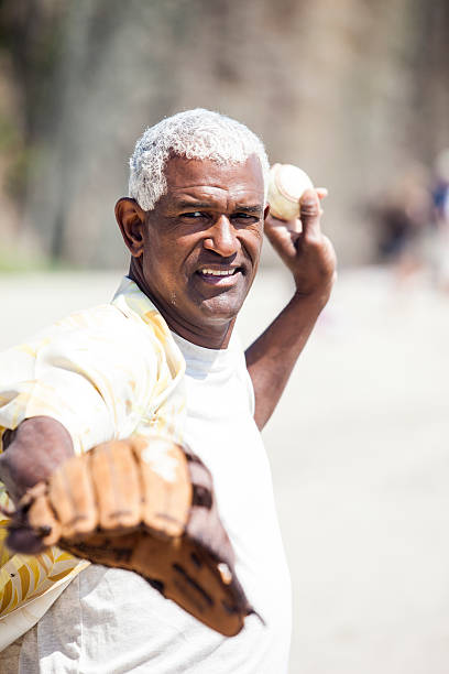 African American Senior Man Playing Baseball Catch African American Senior Man Playing Catch on beach with baseball glove and baseball, throwing the ball to somebody who is off-camera. old baseball stock pictures, royalty-free photos & images