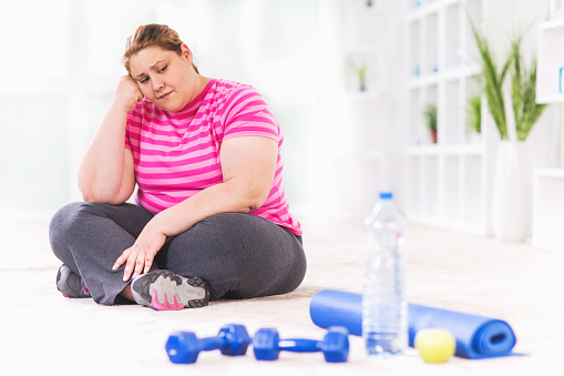 Depressed overweight woman sitting on the floor and doesn't wont to exercise.   