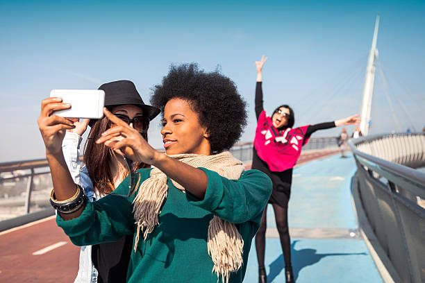 Two friends victim of "photo bombing" taking a selfie Two friends while taking a selfie on mobile phone are victim from another woman of "photo bombing". The photo bombing is when intentionally posing in other people's photos, for a later surprise.  photo bomb stock pictures, royalty-free photos & images
