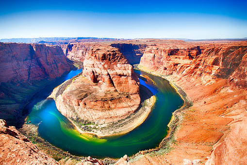 Horseshoe Bend at the Colorado River in hues of bright orange, greens, blues and yellows. This natural attraction is located in Page Arizona. Taken with a 5D mark 3 Camera.