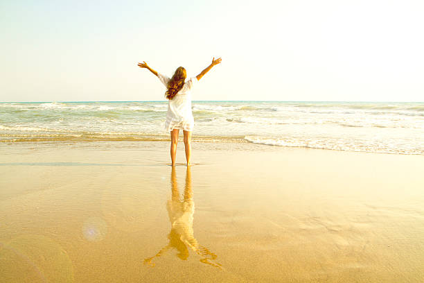 cheering woman open arms under sunrise on beach