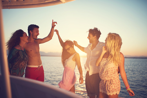 Group of friends having fun on a boat at sunset while dancing.