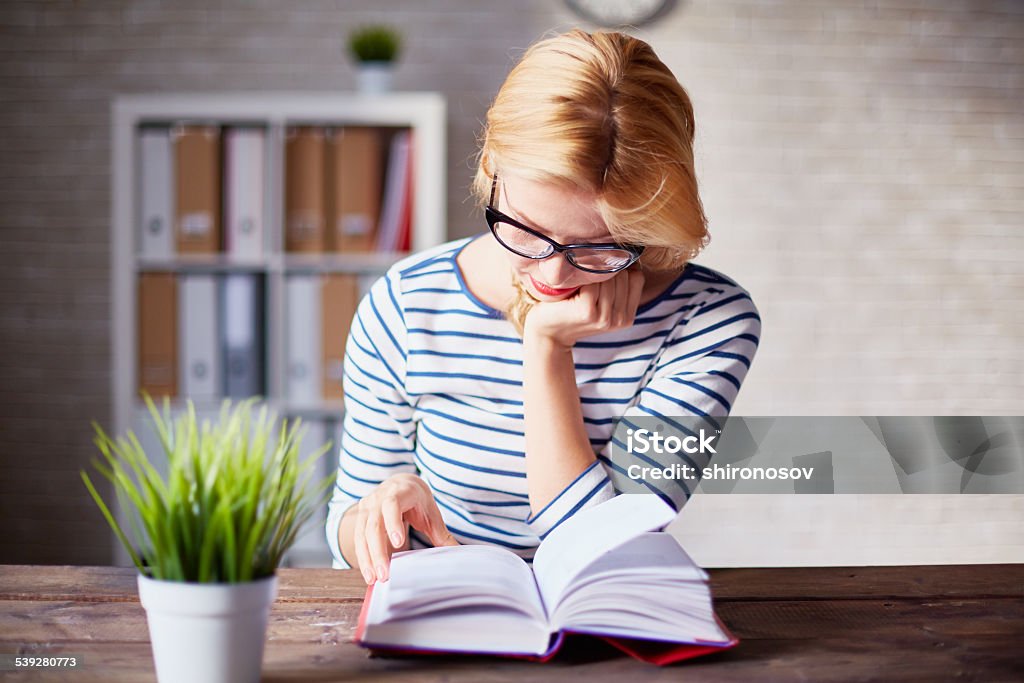 Reading book Charming girl sitting by wooden table and reading book Adult Stock Photo