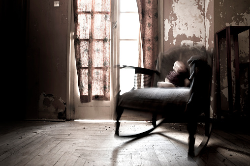 Motion blur of rocking chair with a doll sitting on it in an old dirty room