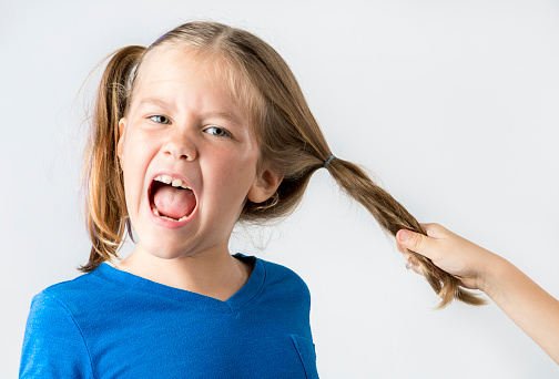 A young girl having her hair pulled.